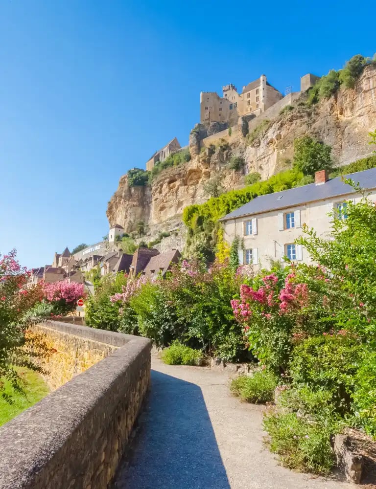 Cycling route through a scenic Dordogne village with stone houses, lush greenery, and pink flowering trees