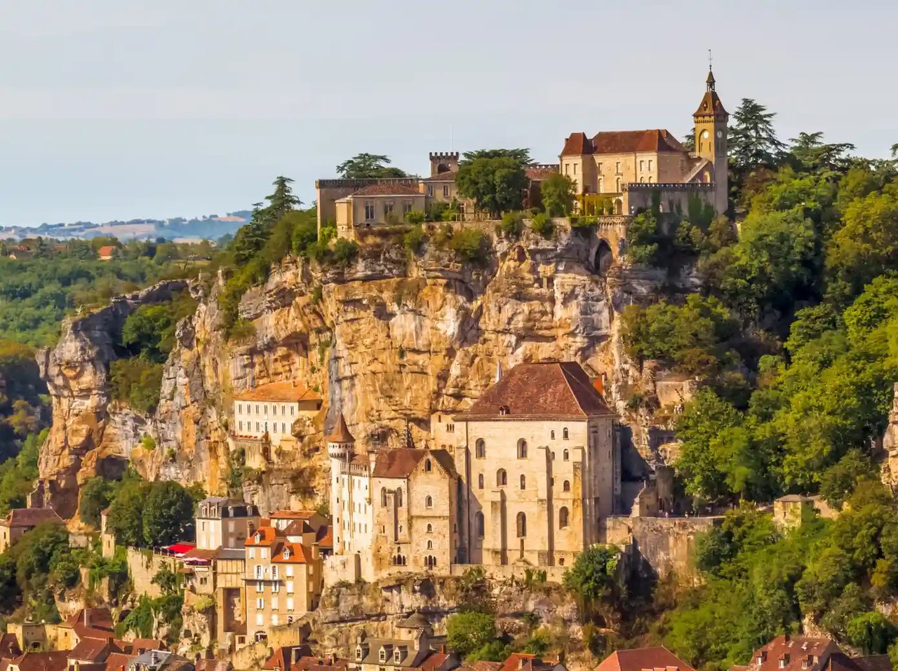 Historic cliffside village in the Dordogne, France, with stone buildings and a church perched above the valley, showcasing the region’s enchanting villages on a cycling holiday.